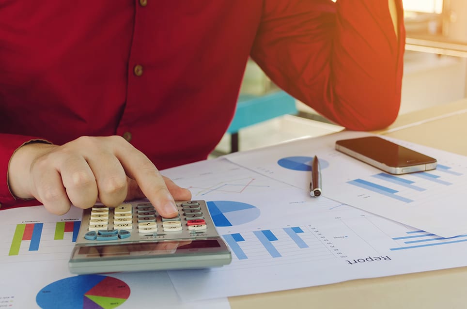 Person-calculating-on-calculator-with-graph-charts-on-the-table Person calculating on calculator with graph charts on the table